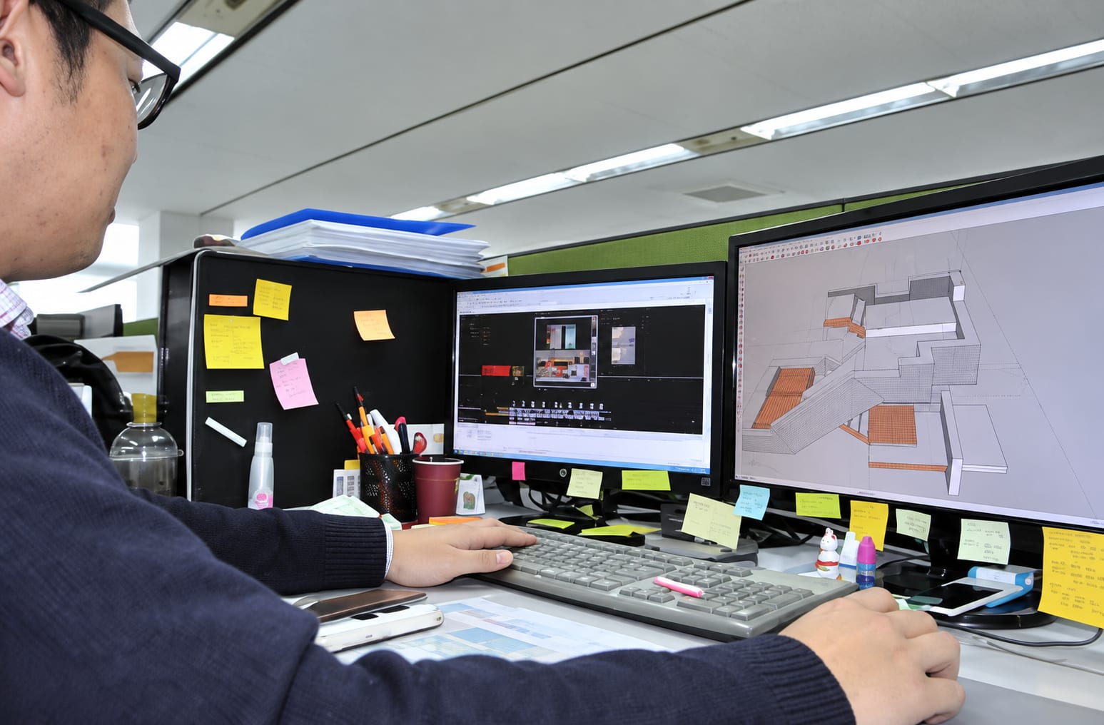 Projetista trabalhando em dois monitores com o modelo 3D de uma edificação no software CAD